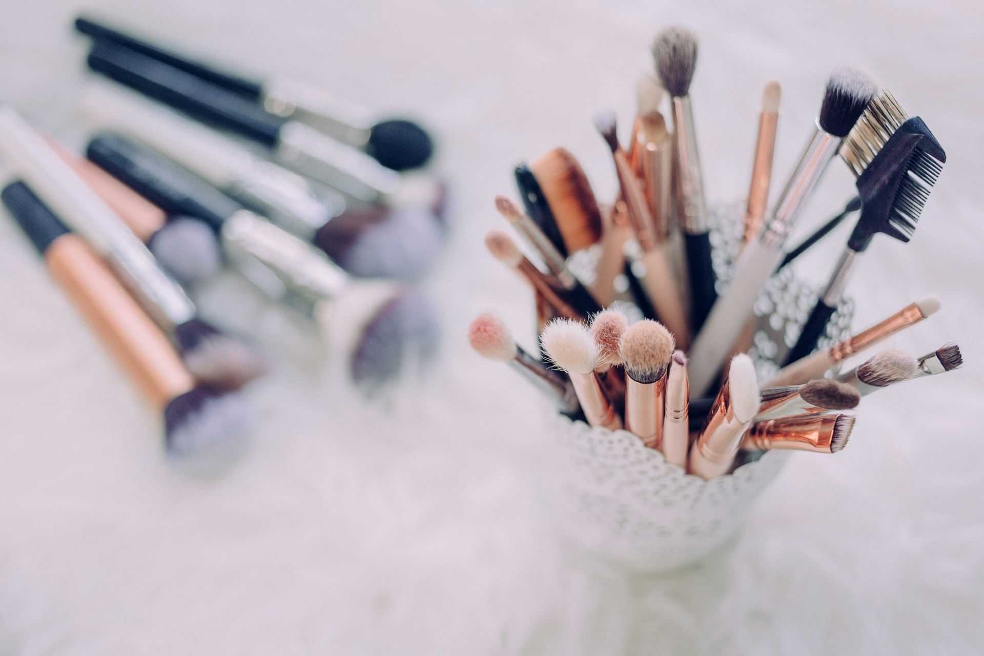 Makeup brushes in a decorative holder on a soft, white surface.