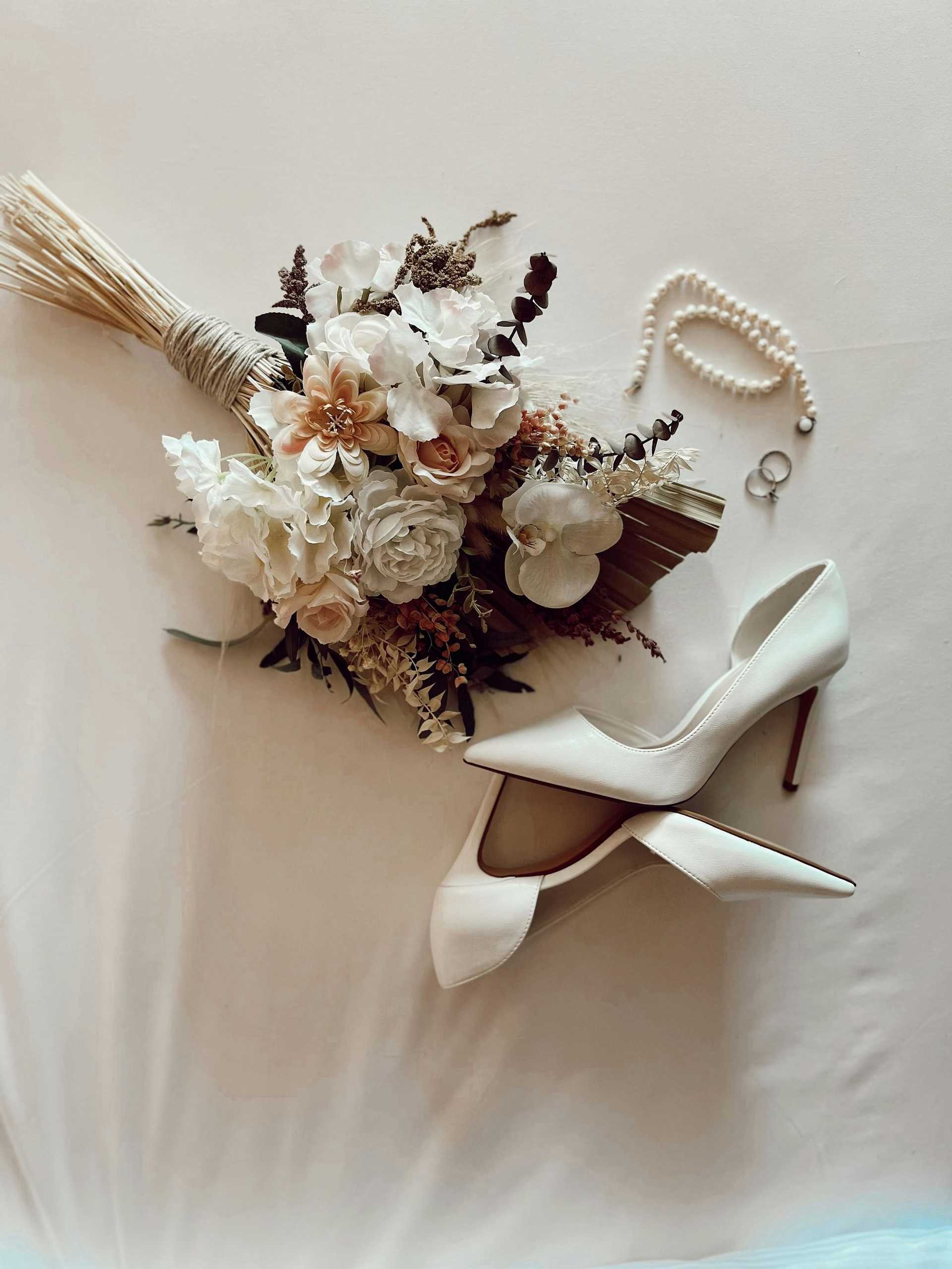 Bridal accessories: bouquet, high heels, pearl necklace, and rings on display.
